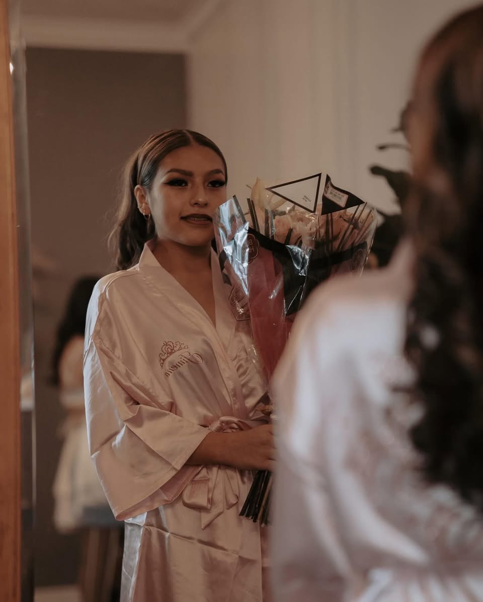 Quinceañera in robe holding bouquet with full glam by MakeupByGen